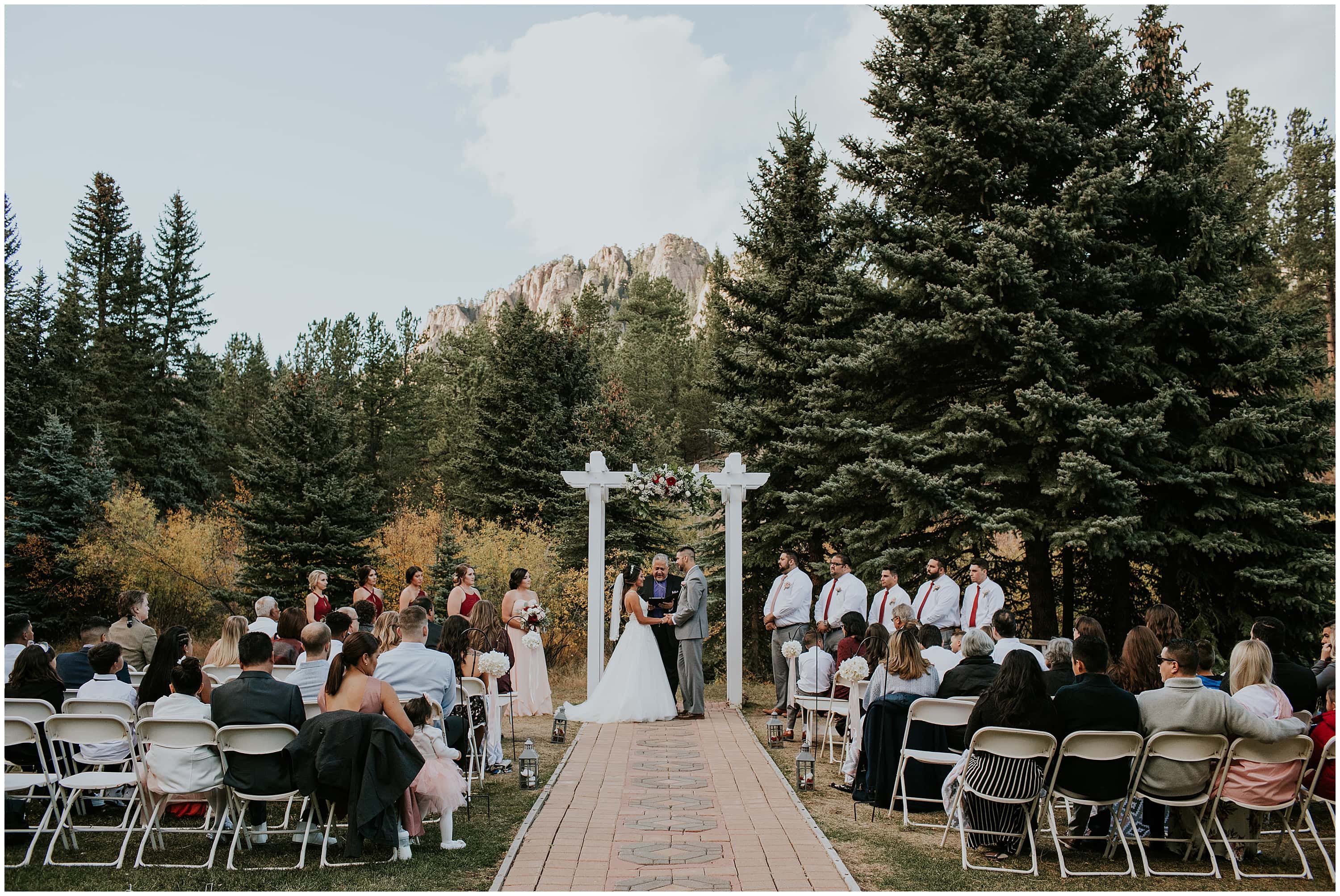 Monutain View Ranch Wedgewood Wedding Photographer, Monutain View Ranch Wedgewood Fall Wedding Photographer, Mountain View Ranch, Fall Mountain wedding, Colorado mountain wedding, Wedgewood weddings, Fall wedding, hispanic couple, reception group photo, Outdoor mountain ceremony, Colorado outdoor ceremony, fall outdoor ceremony, converse shoes, cake cutting, bird cake topper, red & pink bridesmaids dresses, grey grooms suit